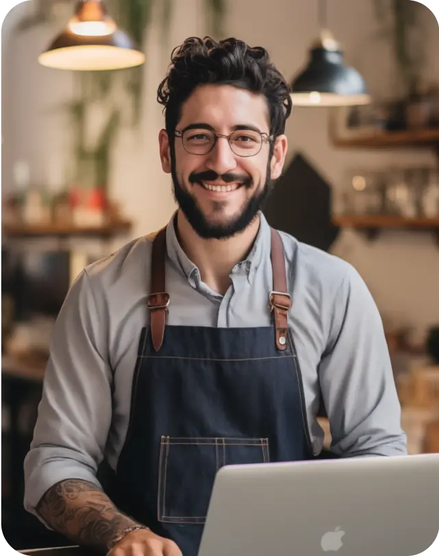Cheerful shop owner working on a laptop in a cafe environment